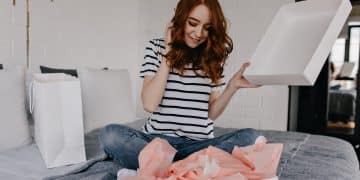 Dreamy girl in striped t-shirt sitting on bed. Ecstatic red-haired curly woman posing in bedroom